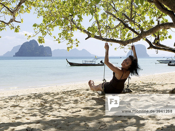 Junge Frau auf einer Schaukel unter einem blühenden Baum am Strand der Insel Ko Hai  Ko Ngai  Andamanensee  Provinz Satun  Südthailand  Thailand  Asien