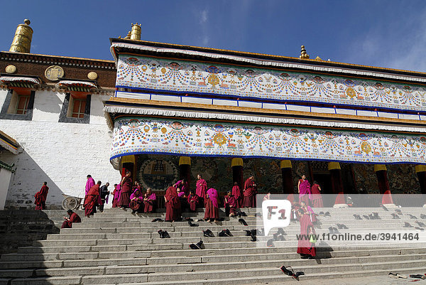 Tibetische Mönche in Mönchsrobe des Gelukpaordens sitzen auf den Treppen vor der Versammlungshalle  tibetisch Dukhang  des Kloster Labrang  Xiahe  Gansu  China  Asien