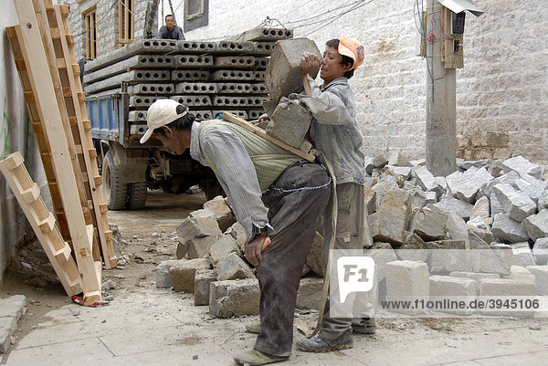 Harte Arbeit  Männer  tibetische Bauarbeiter wuchten und schleppen schwere Steine auf dem Rücken  Altstadt von Lhasa  Himalaya  Autonomes Gebiet Tibet  Volksrepublik China  Asien