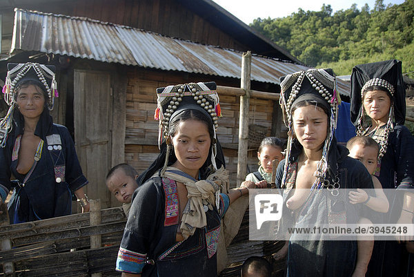 Armut Frauen der Akha Nuqui Ethnie Kleinkinder auf dem Rücken Tracht traditionelle Kleidung Farbe Indigo Kopfbedeckung mit Silber-Schmuck vor Hütte Dorf Ban Seochayneua Provinz und Distrikt Phongsali Laos Südostasien Asien