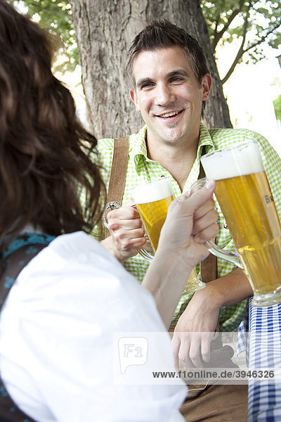 Young couple wearing the traditional costume  a dirndl  drinking beer in a Bavarian beer garden in Regensburg  Bavaria  Germany  Europe