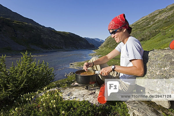 Young woman preparing a meal  cooking outdoors  MSR fuel stove  Happy Camp  historic Chilkoot Trail  Chilkoot Pass  Long Lake behind  Yukon Territory  British Columbia  B. C.  Canada