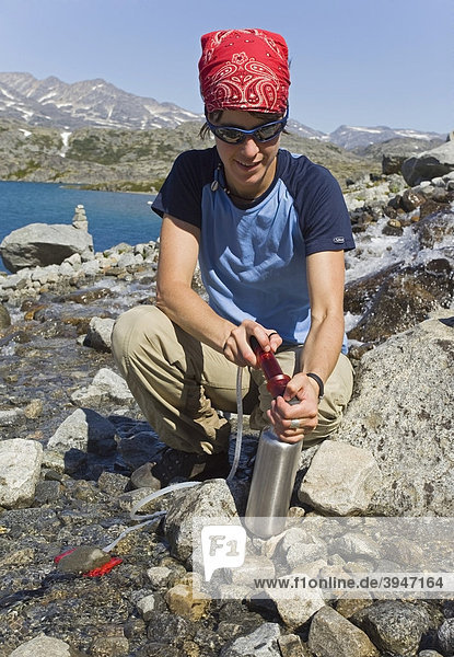Young woman  hiker filtering fresh  potable water from a creek  Purification  protection from Giardia  historic Chilkoot Pass  Chilkoot Trail  Crater Lake behind  alpine tundra  Yukon Territory  British Columbia  B. C.  Canada