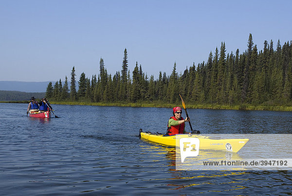 Young woman in kayak  paddling  kayaking  canoe behind  Caribou Lakes  upper Liard River  Yukon Territory  Canada