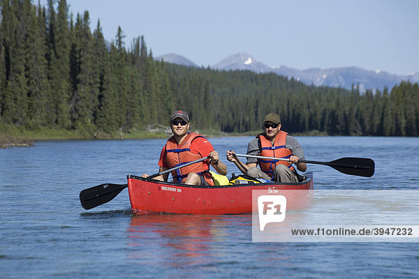 Zwei junge Männer in einem Boot  Kanu  Paddeln auf dem oberen Liard River Fluss  dahinter die Pelly Mountains Berge  Yukon Territory  Kanada