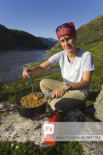 Young woman preparing a meal  cooking outdoors  MSR fuel stove  Happy Camp  historic Chilkoot Pass  Chilkoot Trail  Long Lake behind  Yukon Territory  British Columbia  B. C.  Canada