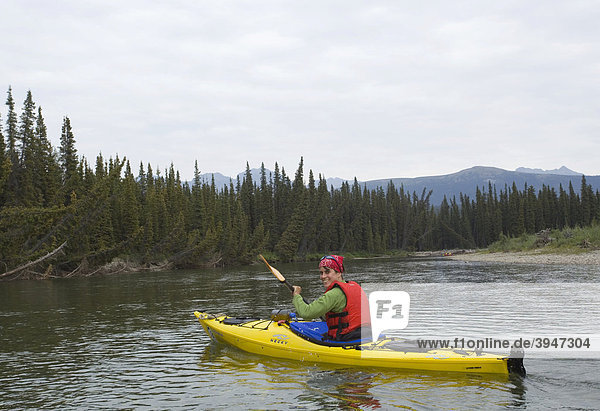 Young woman paddling a kayak  kayaking  upper Liard River  Pelly Mountains behind  Yukon Territory  Canada