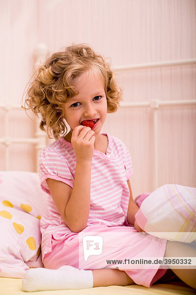 Siebenjähriges Mädchen isst Erdbeere im Bett