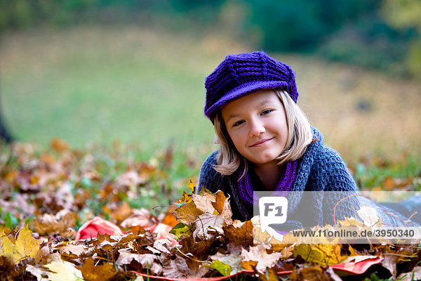 Dreizehnjähriges Mädchen liegt zwischen bunten Blättern im Herbstpark