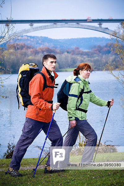 Couple hiking beside a lake in front of a railway bridge