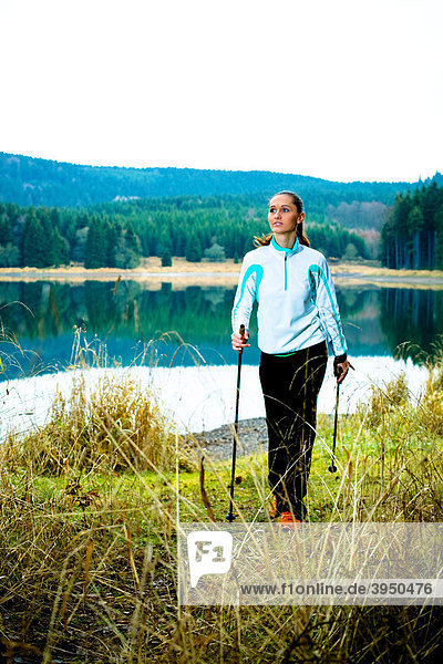 Junge Frau wandert am See im Nordic Walking Stil