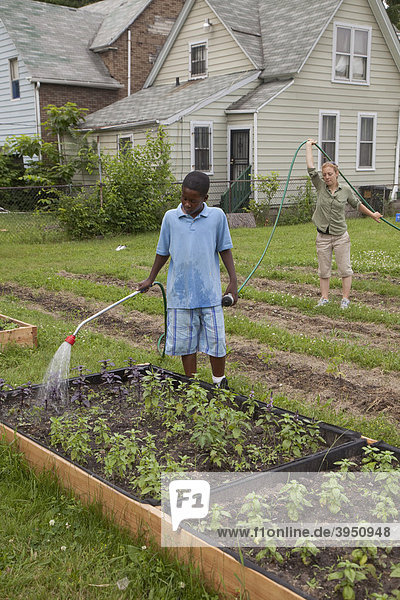 Ein Junge wässert Pflanzen  unterstützt von einer Aufsichtsperson  in einem Programm namens Growing Healthy Kids für Kinder im Alter von 5-11 Jahren  in einem Earthworks Urban Garden Garten  in dem Nahrung für die Capuchin Soup Kitchen Suppenküche angebaut wird  Detroit  Michigan  USA