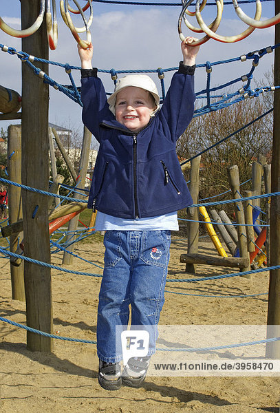 Kleiner Junge  2 Jahre  hängt an Ringen auf einem Spielplatz