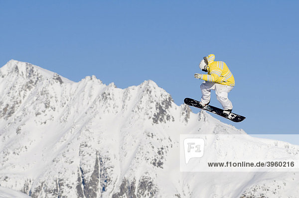 Skifahrer beim Sprung vor blauem Himmel  dahinter schneebedeckte Bergkette  Andermatt  Schweiz
