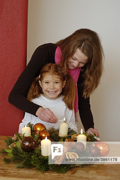 Junge Frau mit Kind zündet Kerzen an einem Adventskranz an
