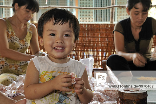 Kleines Kind lacht und isst Puffreis-Süßigkeiten  Süßwarenfabrik  Vinh Long  Mekongdelta  Vietnam  Südostasien