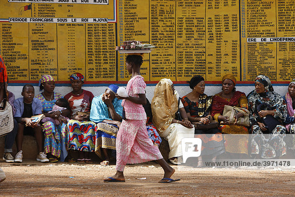 Mädchen verkauft Imbiss  Frauen vor dem Sultanspalast  warten auf Audienz beim Sultan  dahinter Tafeln zur Geschichte der Bamundynastie  Foumban  Kamerun  Afrika