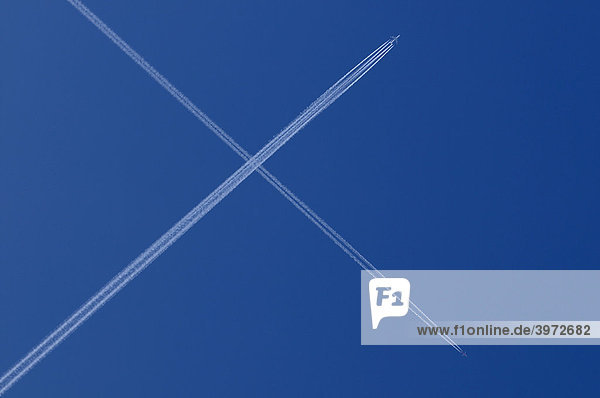 Zwei Flugzeuge mit Kondensstreifen kreuzen sich am blauen Himmel  X