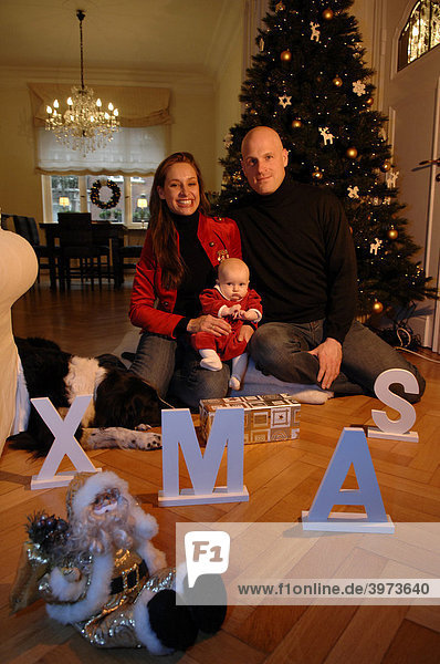 Familie mit Baby an Weihnachten in ihrem geschmückten Wohnzimmer