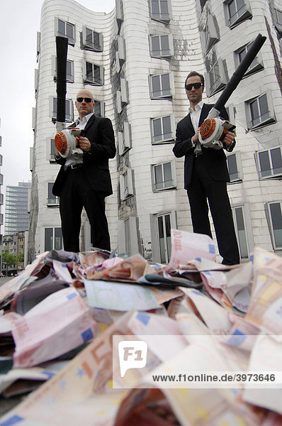 Men in Black  zwei Businessleute mit Laubbläsern und Geldscheinen  Symbolfoto zum Thema Geldverschwendung