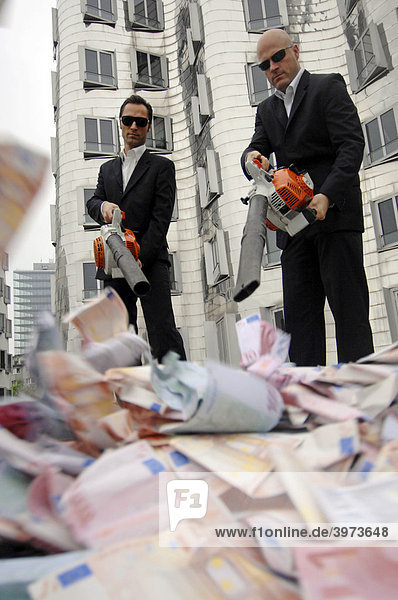 Men in Black  zwei Businessleute mit Laubbläsern und Geldscheinen  Symbolfoto zum Thema Geldverschwendung