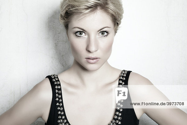 Portrait of a young blond woman in front of a white wall looking at the viewer