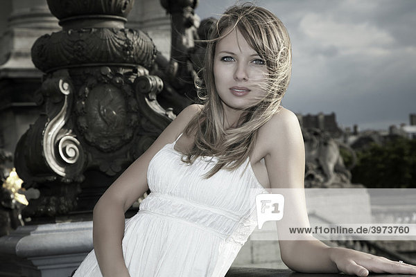 Portrait of a young dark blonde woman in a white dress leaning on the railing of the Alexander Bridge  Paris  France  Europe