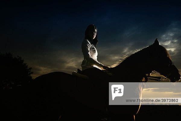 Young woman riding her horse in the sunset