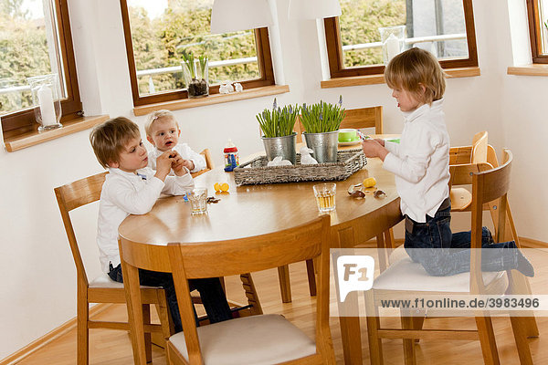 Three children  1  3 and 6 years old  sitting at the table and eating sweets