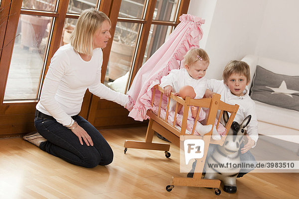 Mutter mit zwei Kindern  1 und 6 Jahre  spielen mit Puppenwagen und Hüpftier