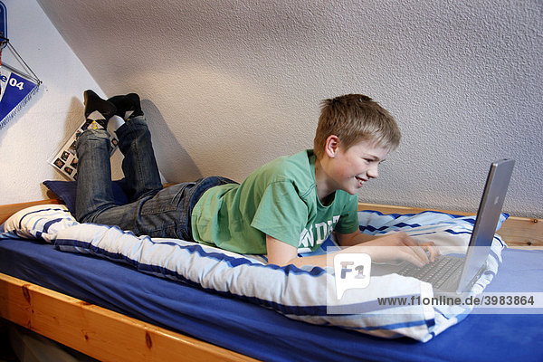 Boy  13  working with his computer at home in his bedroom while lying on his bed