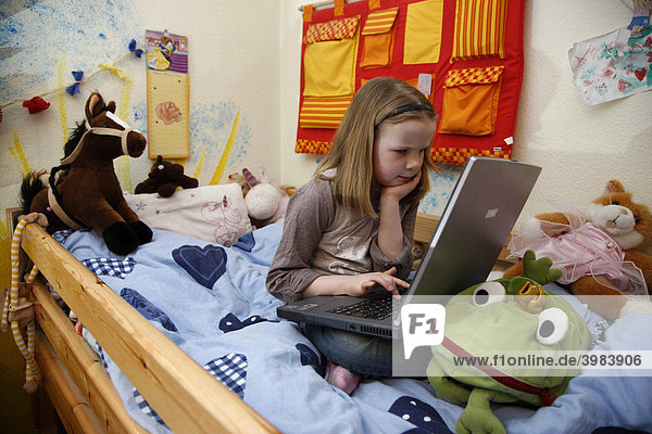 Mädchen  7 Jahre  arbeitet mit einem Computer zuhause im Kinderzimmer  sitzt auf ihrem Etagenbett  macht Hausaufgaben für die Schule  Lernsoftware