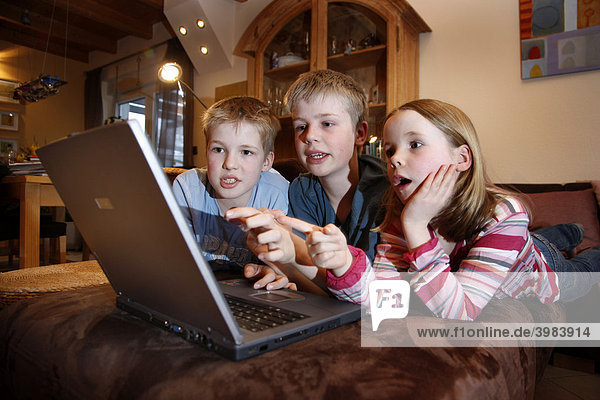 Siblings  7  11  13 years old  with laptop computer  in the living room  playing an educational game quiz