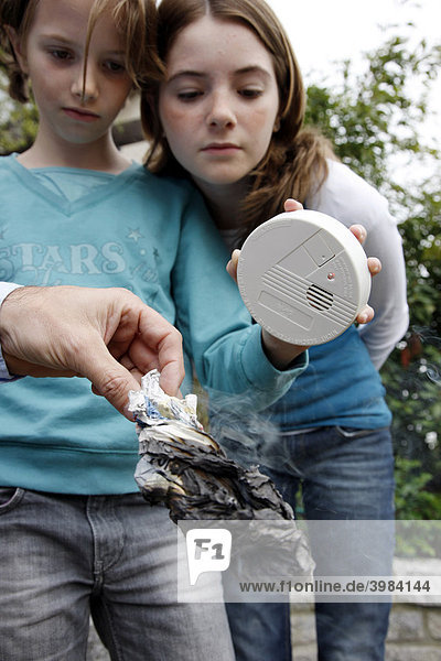 Mädchen wird die Funktion eines Rauchmelders demonstriert  mit Hilfe eines brennenden  qualmenden Stück Papier  Deutschland  Europa