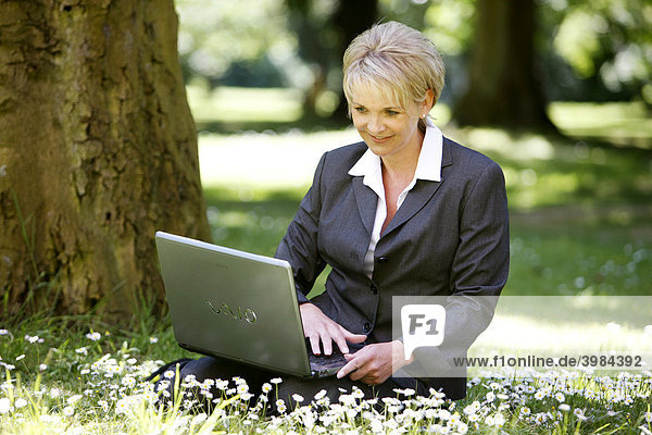 Frau im Business Kostüm  Hosenanzug  Geschäftsfrau  Anfang 40  arbeitet in einem Park an einen Laptop Computer