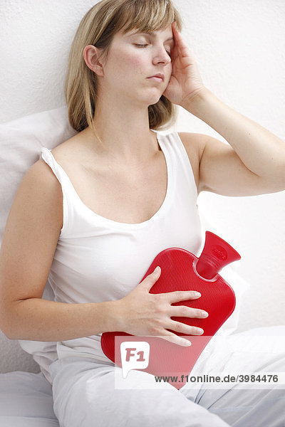 Junge Frau hat Bauchschmerzen  lindert die Beschwerden mit einer Wärmflasche