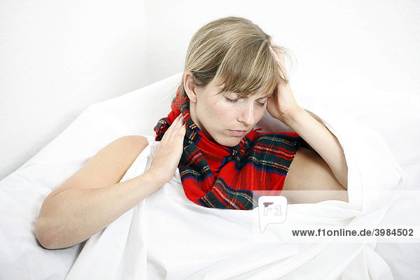 A young woman with a sore throat and a cold in bed  with a scarf
