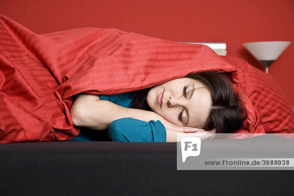 Junge Frau unter roter Bettdecke