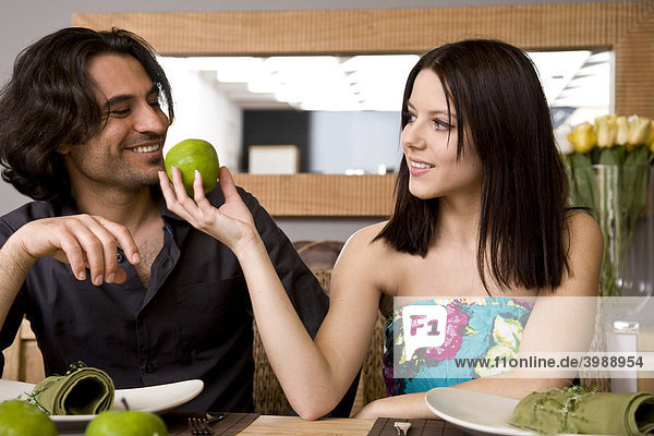 Junges Paar am Esstisch  sie reicht ihm einen Apfel