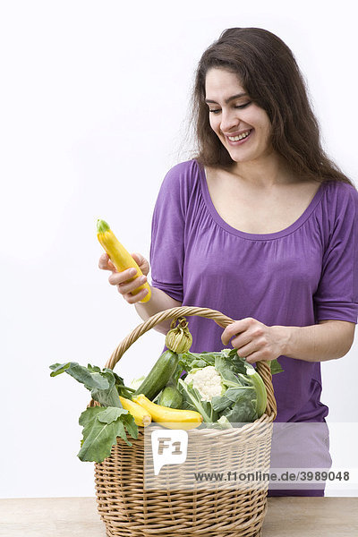 Mädchen blickt auf Gemüsekorb und hält gelbe Zucchini in der Hand