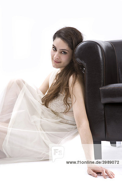Girl with long  dark hair  leaning against leather armchair