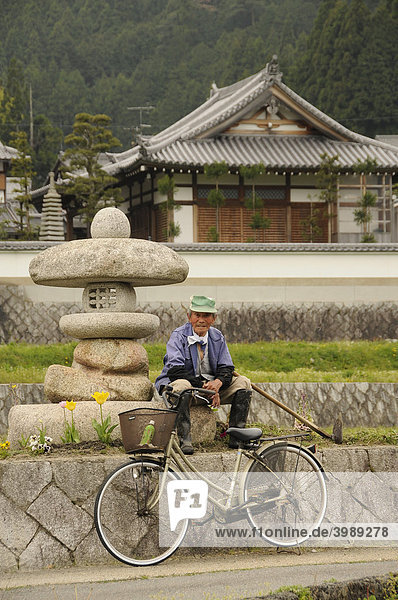 Alter Bauer mit Hacke und Fahrrad vor einer Steinlampe und traditionellem Haus in Ohara bei Kyoto  Japan  Asien