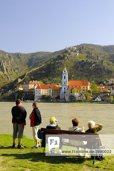 Touristen und Pensionisten auf Sitzbank blicken über die Donau auf Ort und Ruine Dürnstein  Wachau  Niederösterreich  Österreich  Europa