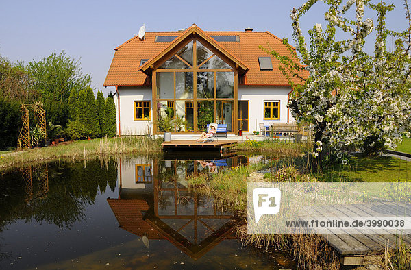 Gartenteich vor Wohnhaus mit Wintergarten und blühendem Kirschbaum