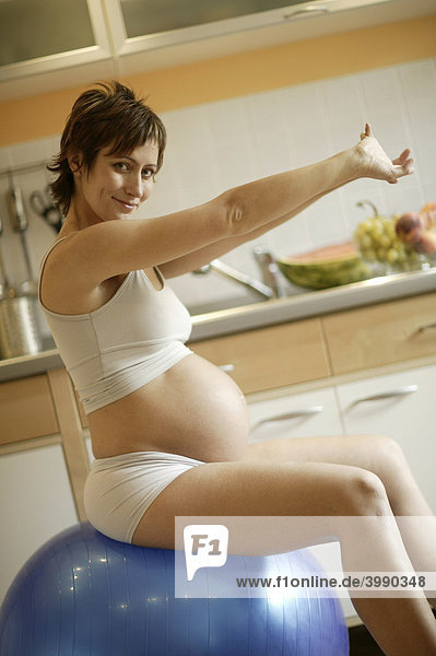 Schwangere Frau macht gymnastische Übungen auf einem Ball sitzend
