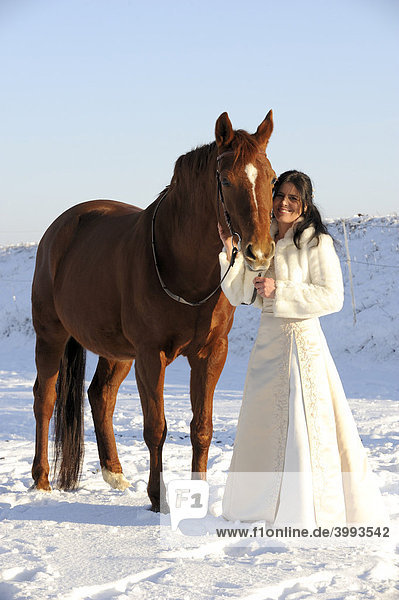 Weiß gekleidete Frau mit Pferd in Winterlandschaft