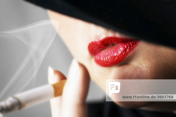 Detail einer Zigarette rauchenden Frau mit roten Lippen und schwarzem Hut mund