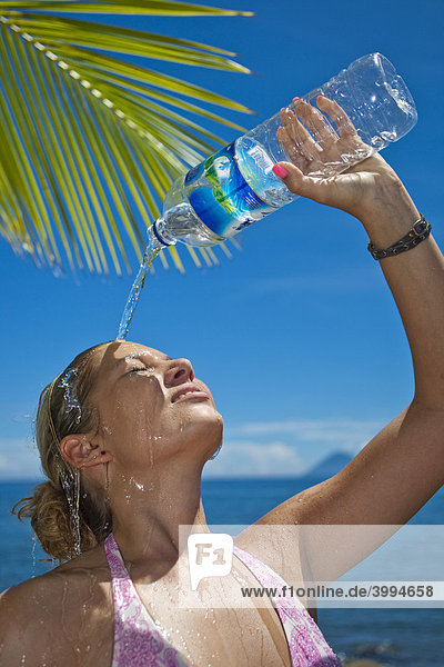 Junge Frau am Strand gießt sich Wasser aus einer Wasserflasche über den Kopf  Indonesien  Südostasien