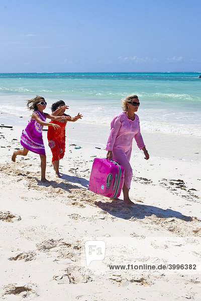 Mother with two children carrying heavy suitcases on the beach
