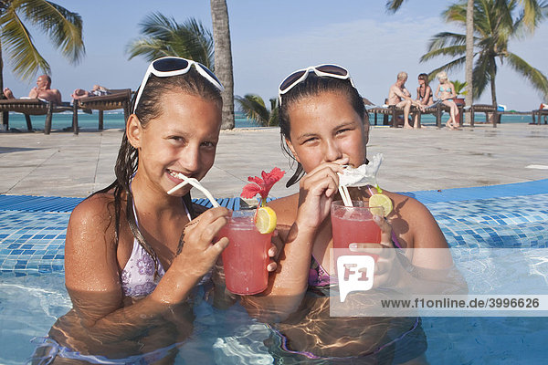 Two girls with sunglasses  about 12 years  drinking cocktails in a swimming pool